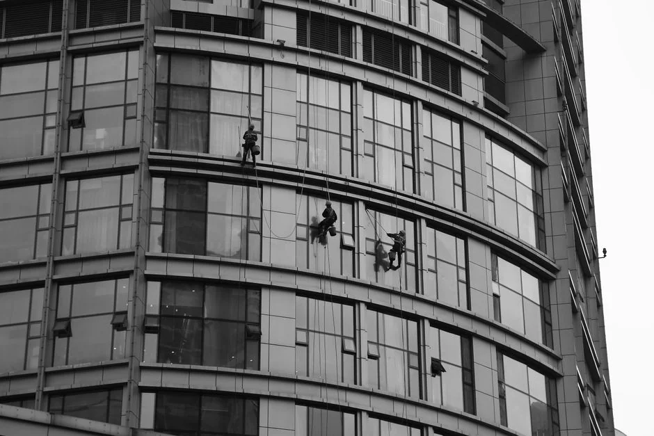 A man cleaning skyscraper windows with a harness, showcasing urban high-rise work.
